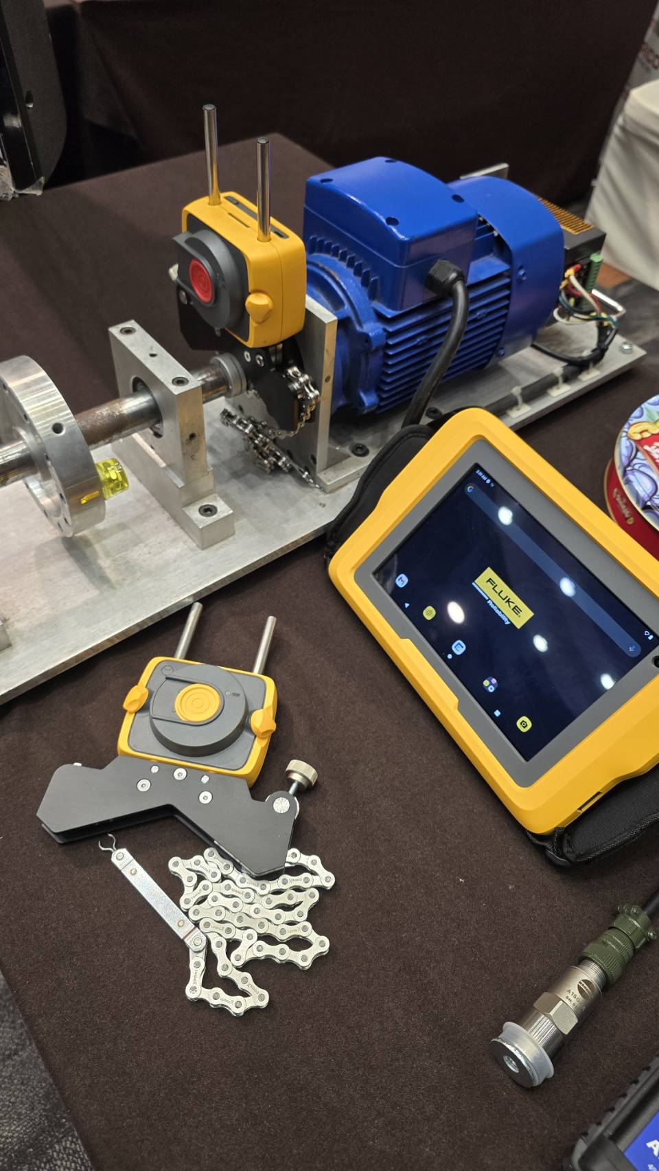 ชุดสาธิตตั้งศูนย์เพลาเลเซอร์ Fluke ประกอบด้วยมอเตอร์ เพลา เซนเซอร์สีเหลืองพร้อมสายโซ่ยึดเพลา และแท็บเล็ต Fluke Reliability บนโต๊ะบูธ MTP-Thai งาน CBM DAY 2026