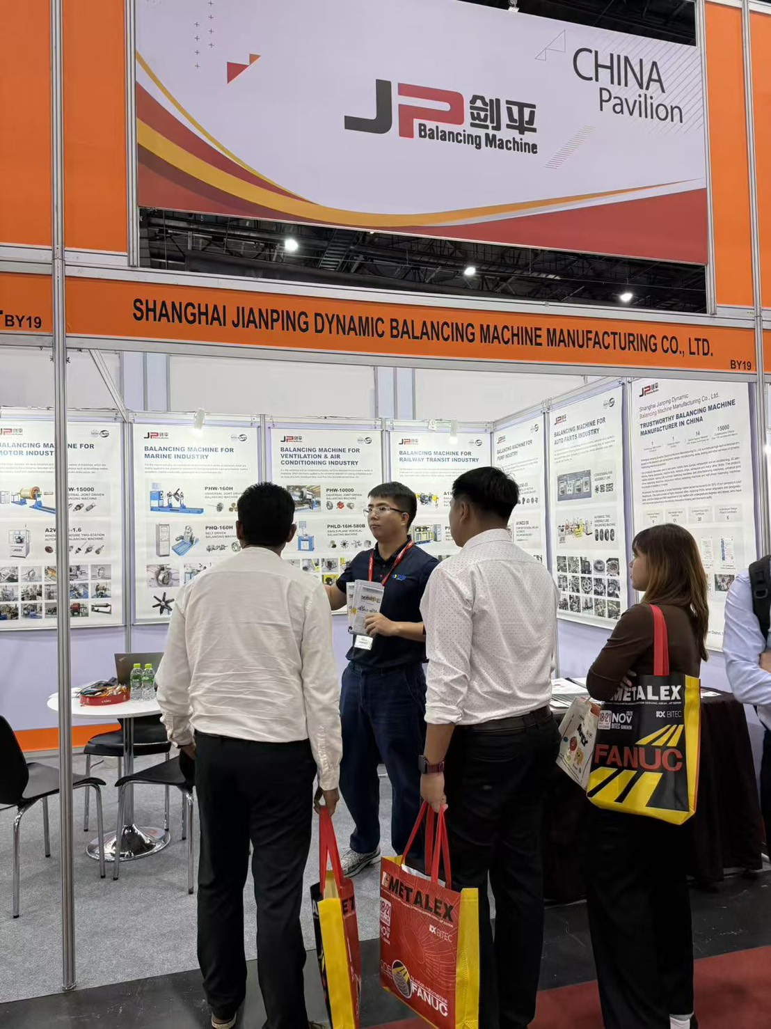 ทีมงานอธิบายเครื่องบาลานซ์ JP ให้ผู้เข้าชมที่บูธ BY19 งาน METALEX 2025 ฉากหลังเป็นป้ายเครื่องบาลานซ์สำหรับอุตสาหกรรมมอเตอร์ เรือ ระบายอากาศ รถไฟ ปั๊ม และชิ้นส่วนยานยนต์