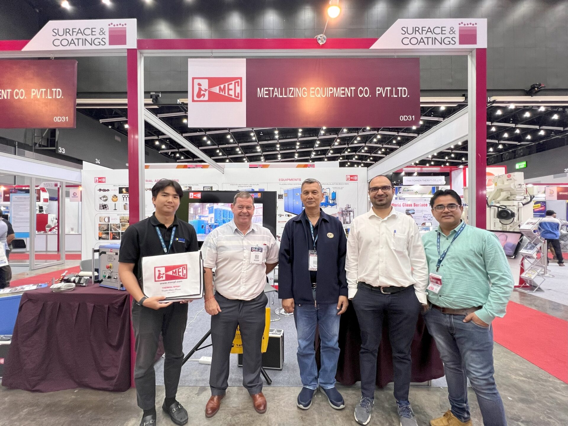 ทีมงาน MTP-Thai และ MEC ยืนหน้าบูธ 0D31 งาน Surface & Coatings 2023 ที่ BITEC ถือถุงผ้า MEC Thermal Spray